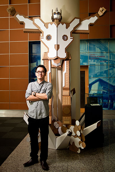Bartholomew Ting standing beside a large cardboard sculpture