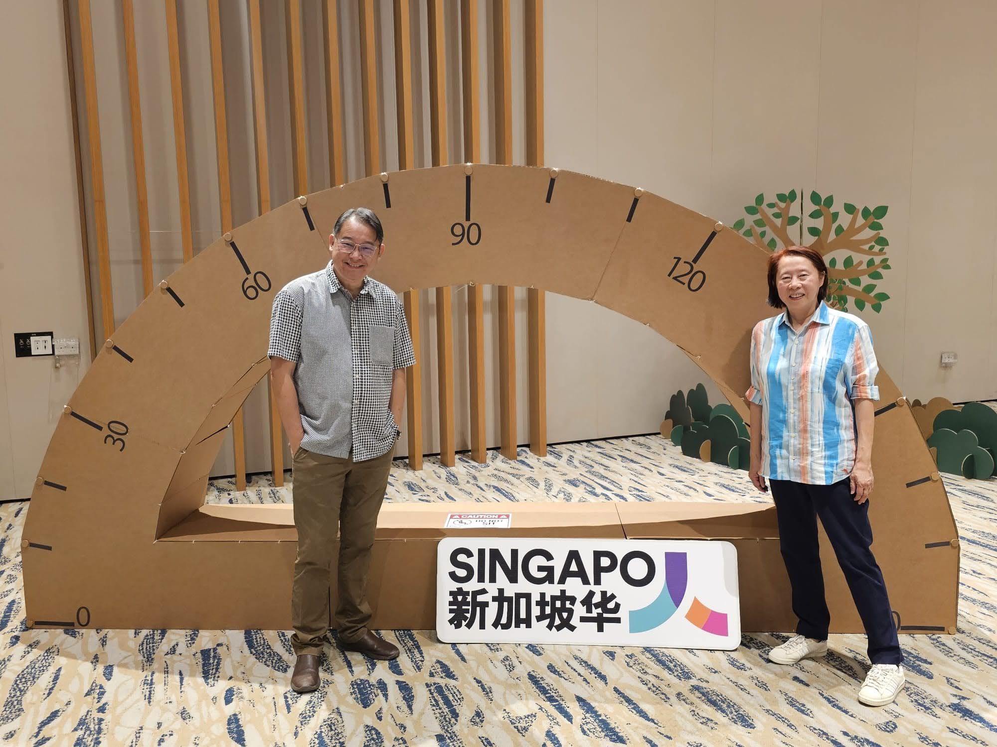 Two visitors standing inside an oversized semicircular cardboard protractor