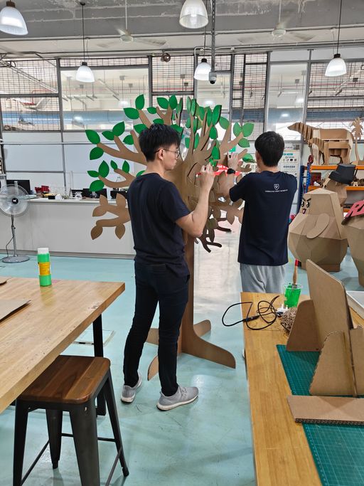 Two makers attaching coloured leaves to a cardboard tree canopy