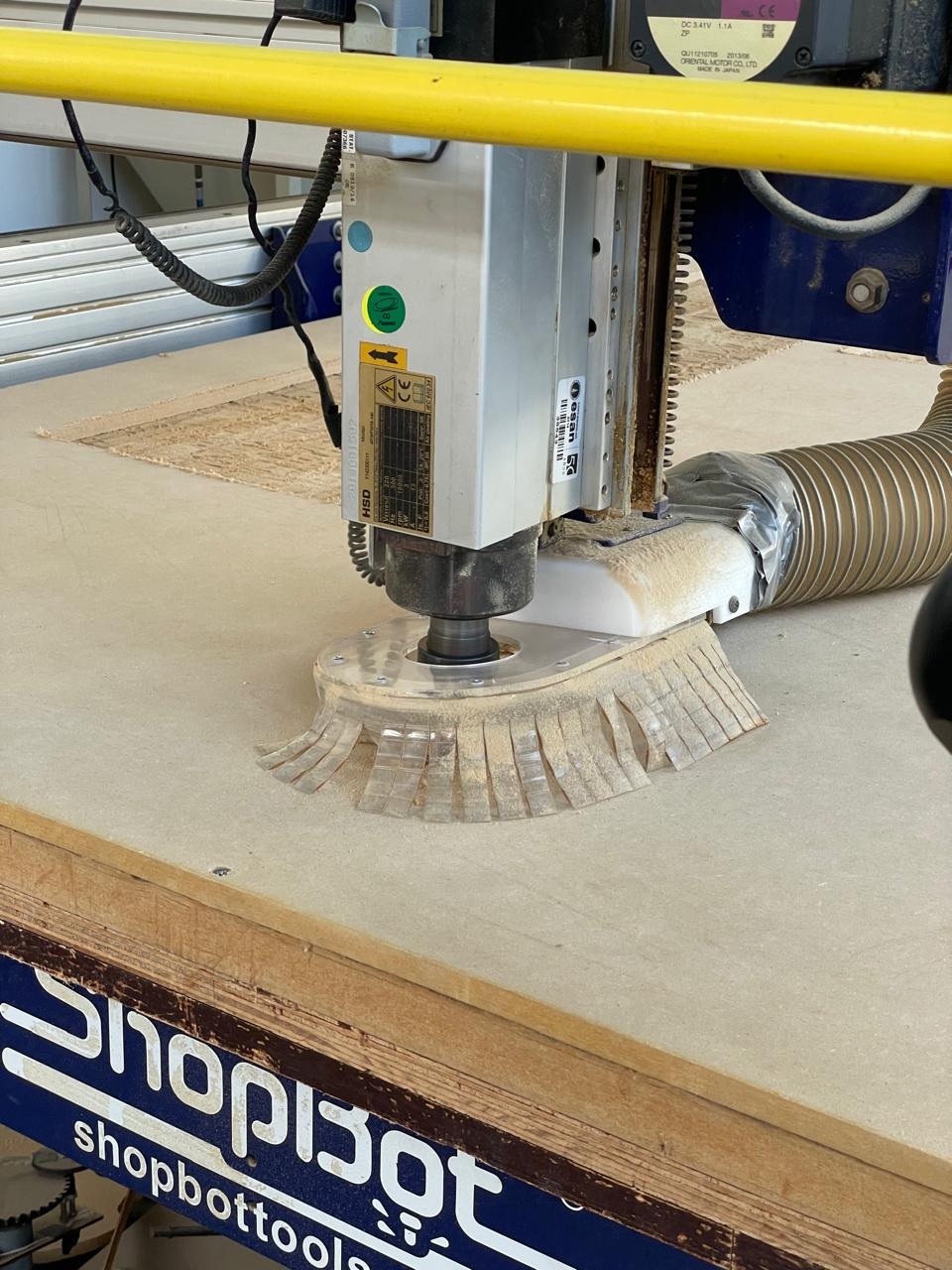 Close-up of the ShopBot HSD spindle with the 1/4 down-cut bit and dust collection skirt — sheet of MDF on the bed