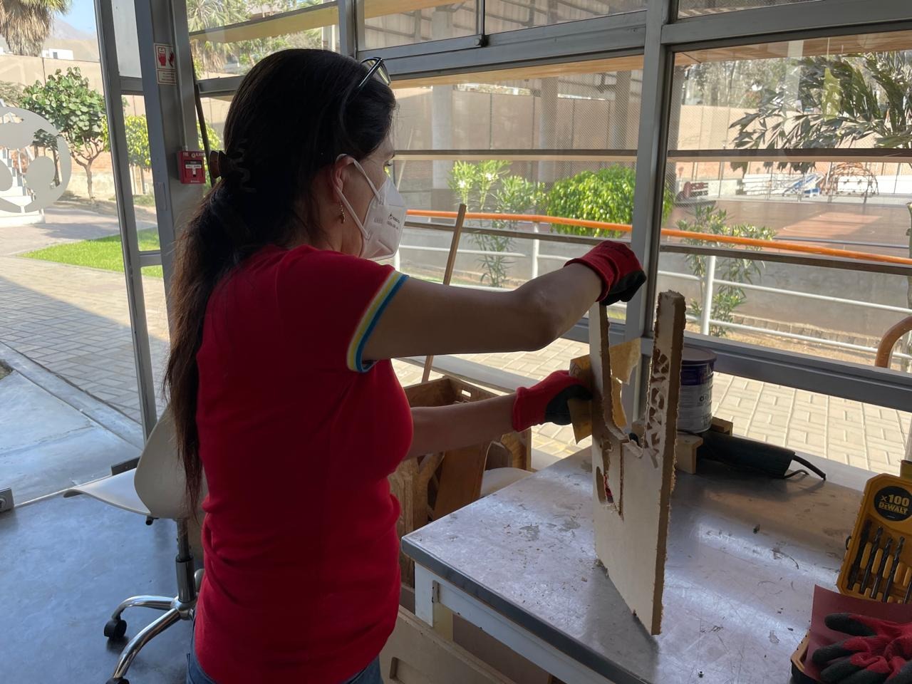 Marita sanding and removing tabs from the bench parts after CNC cutting — dust mask and gloves on