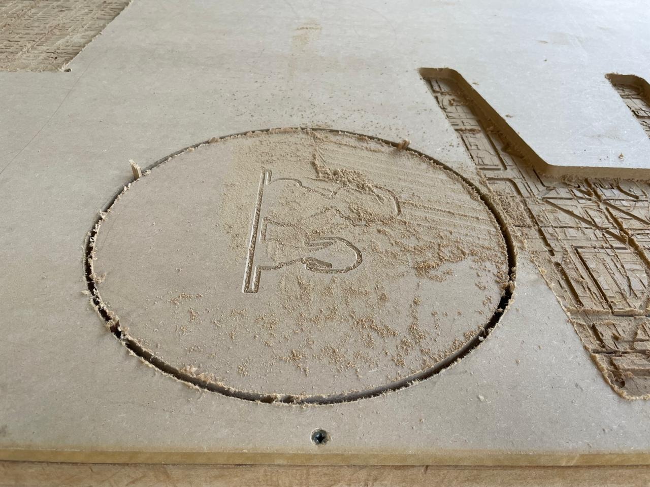 bench top on the ShopBot bed — V-carved Snoopy engraving visible, circular perimeter cut in progress