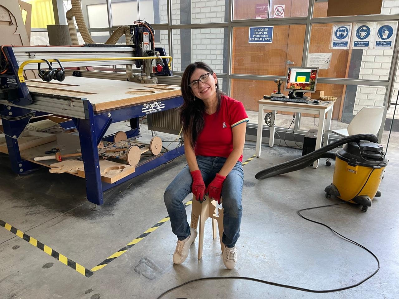 Marita seated on the finished Snoopy bench next to the ShopBot CNC router — ESAN Fab Lab