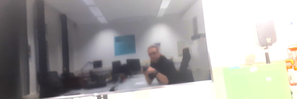 Jakob, sitting at a conference table, reflected in a switched-off TV screen