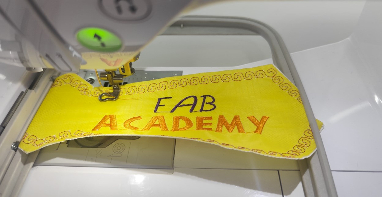 Embroidery machine stitching 'FabAcademy' logo with selected thread colors
