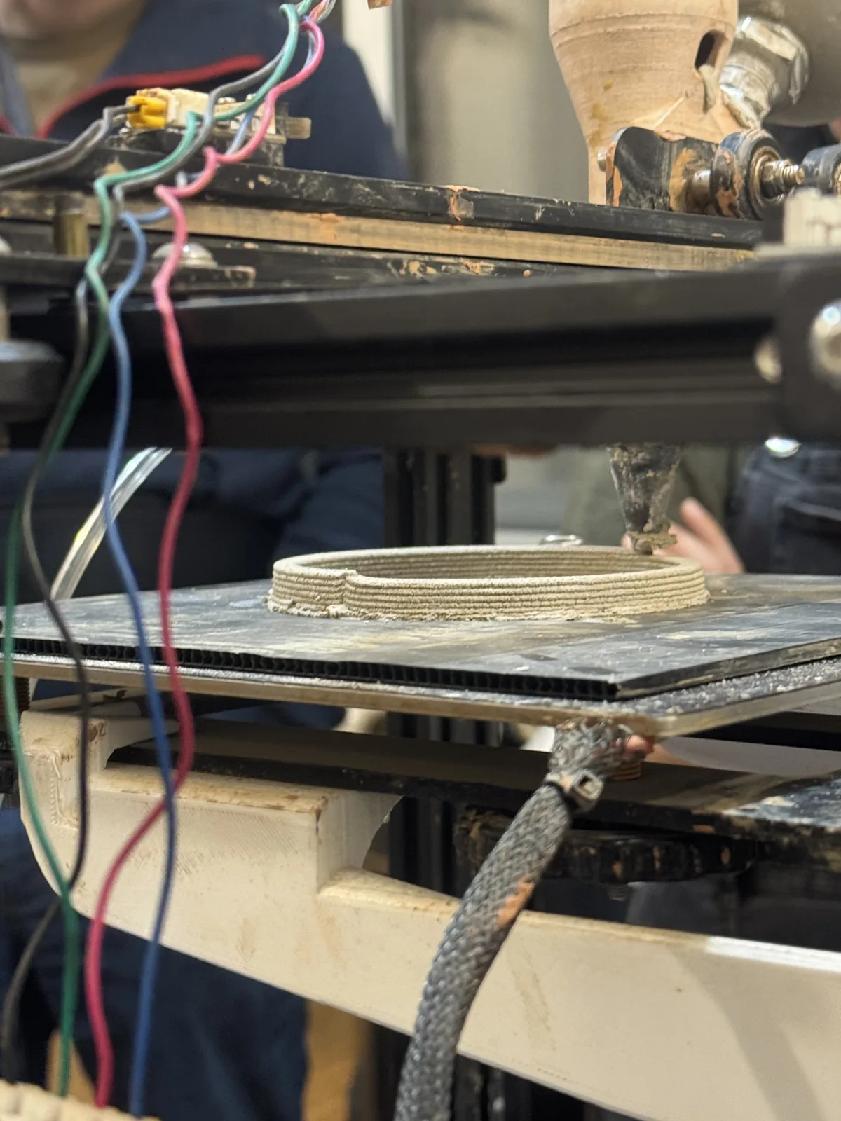 Clay printer extruding a circular coil bead onto the bed, forming the base of a vessel
