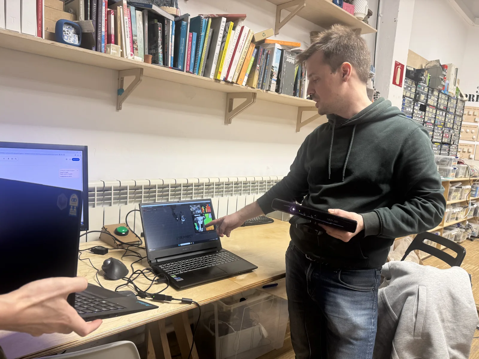 Person holding a handheld 3D scanner connected to a laptop showing a colour point cloud