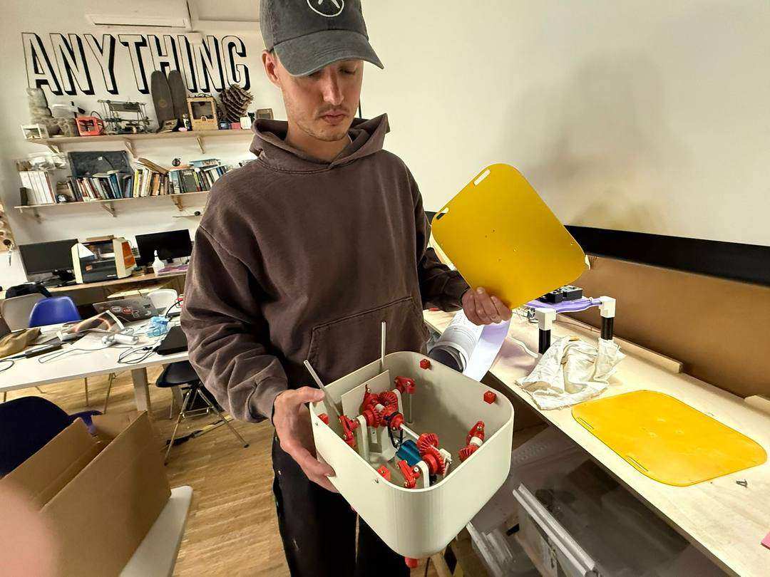 Gabriel holding the assembled creature body with red gears visible inside, yellow acrylic lid in other hand