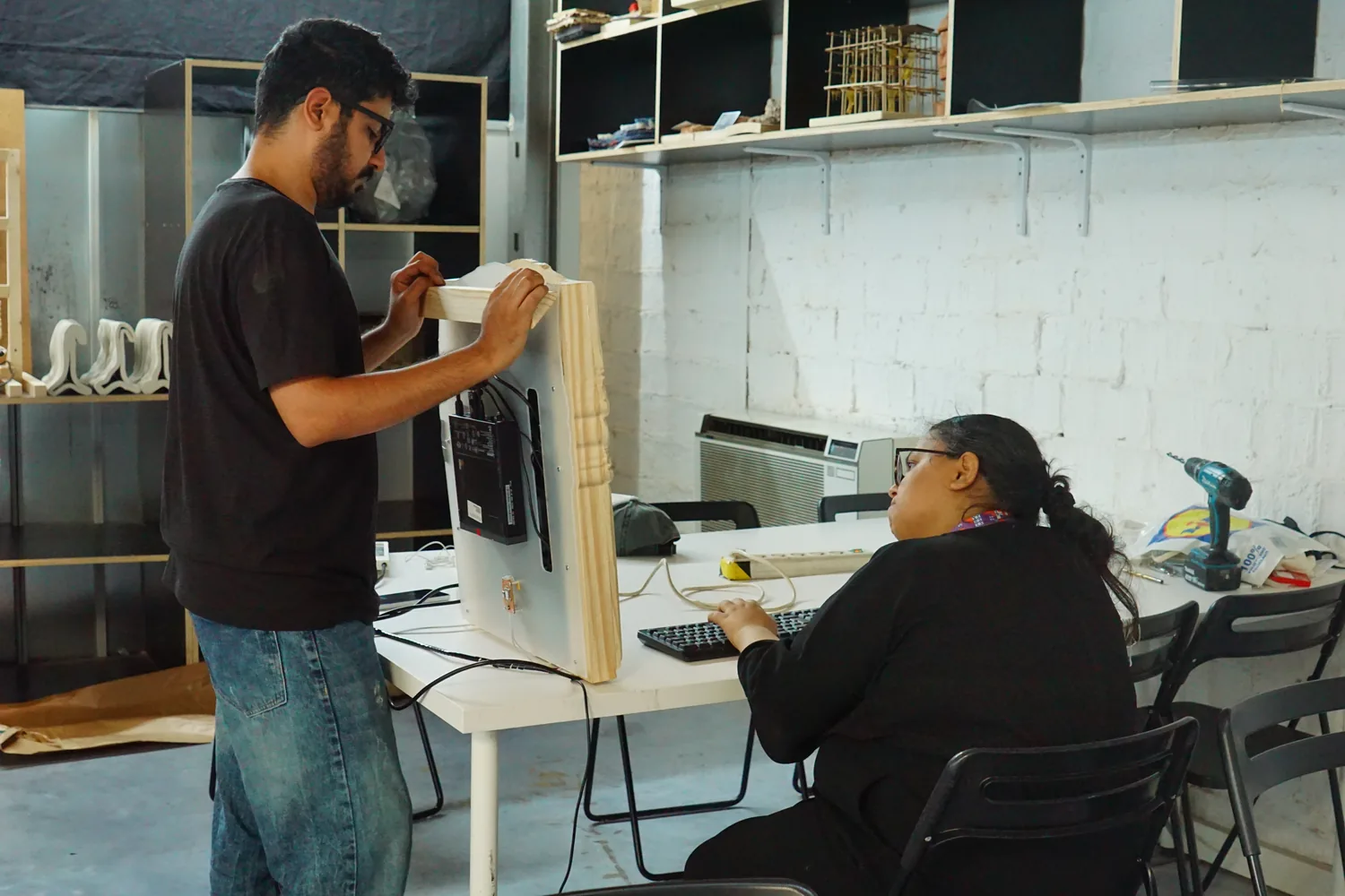 Assembly in progress: one person fitting the carved frame onto the screen stack while another works at a keyboard