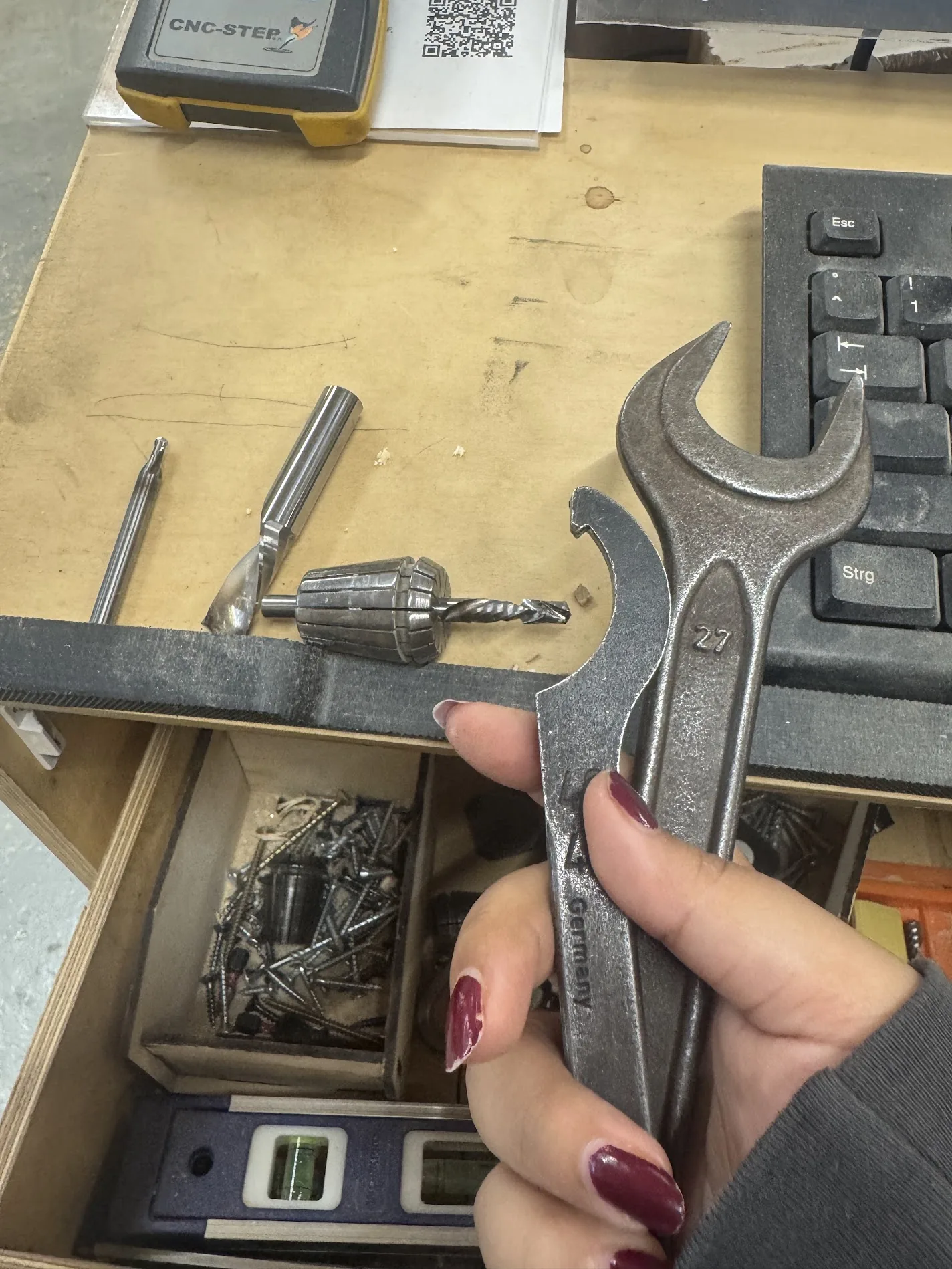 Hand holding a 27 mm collet spanner beside the milling bits used: a small ball mill, a flat end mill, and a drill in a collet, on the CNC-STEP bench