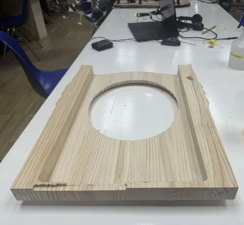 The milled pine back/body panel on a workshop table: an oval aperture cut through the centre and two long channels milled along the sides where the assembly seats