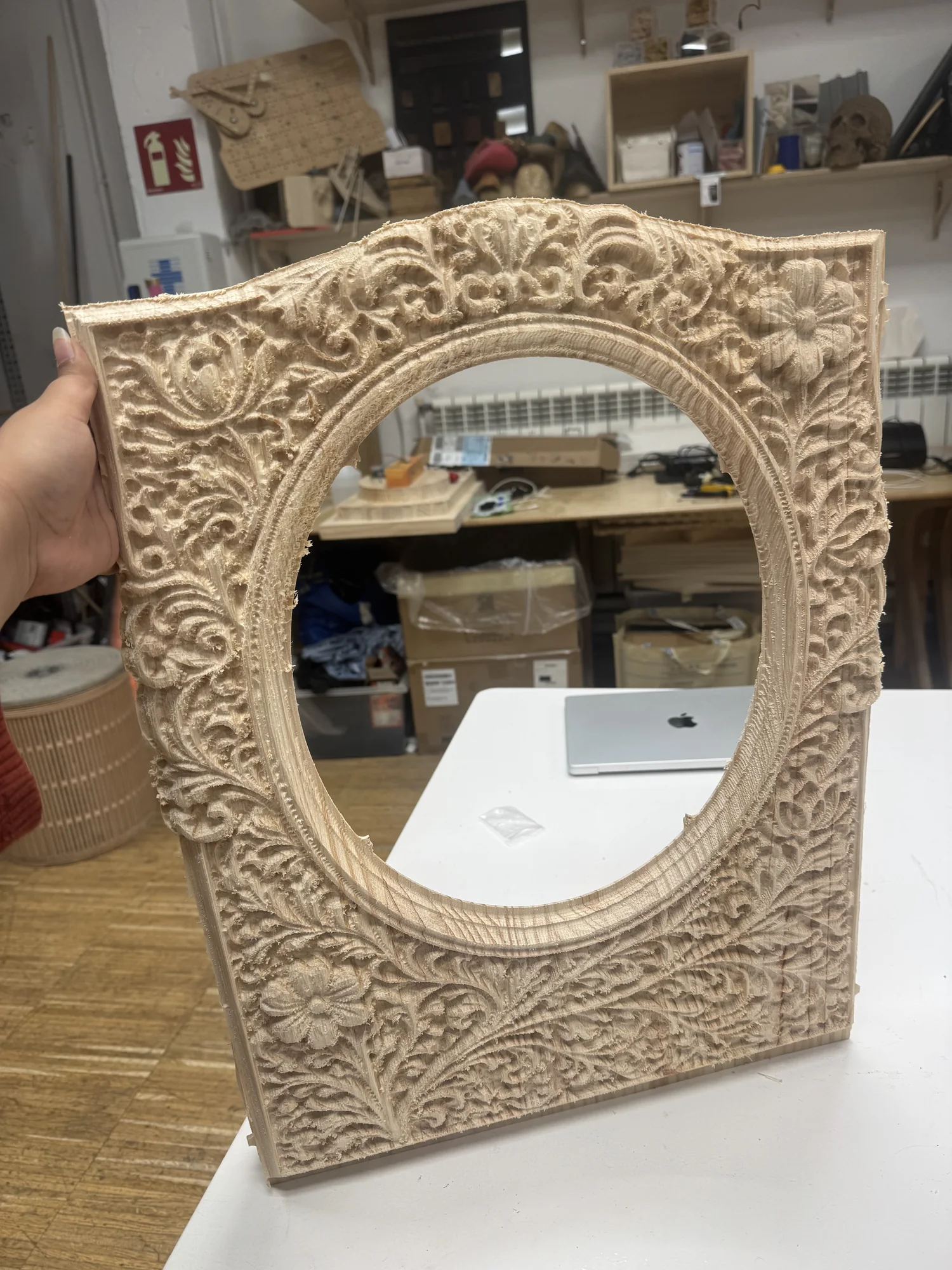 The carved pine frame held up fresh off the CNC: full botanical relief of scrolling vines, leaves and flowers around the oval aperture cut clean through, machining fuzz still on the edges