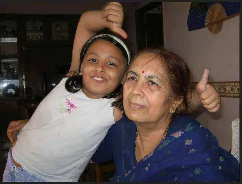 A younger Shiv leaning in beside her grandmother Maya, who smiles and gives a thumbs up