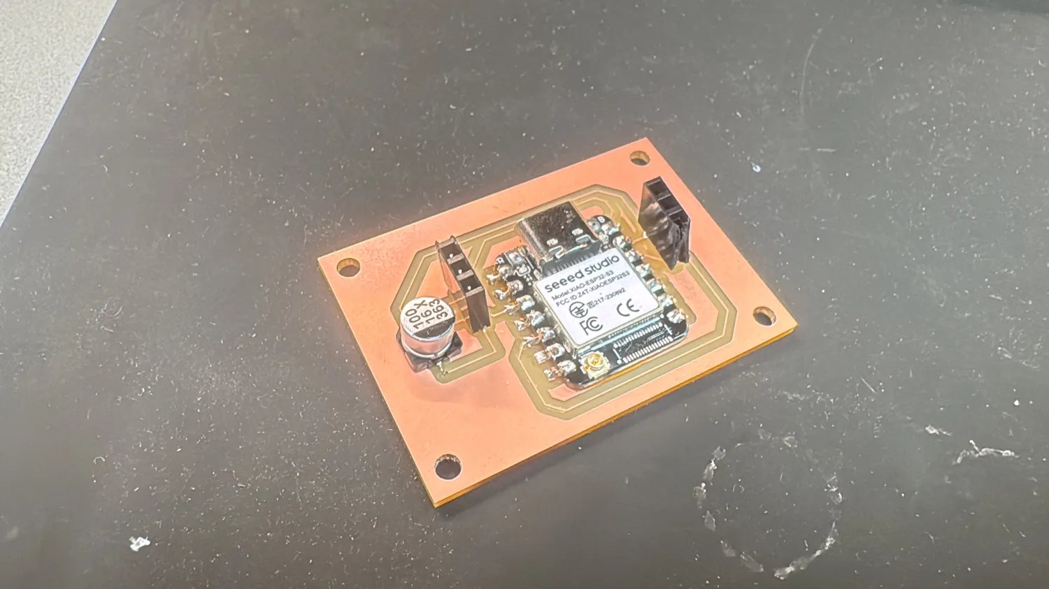 The milled maya board: XIAO ESP32-S3, a 100µF electrolytic cap, and two 3-pin headers on single-sided copper