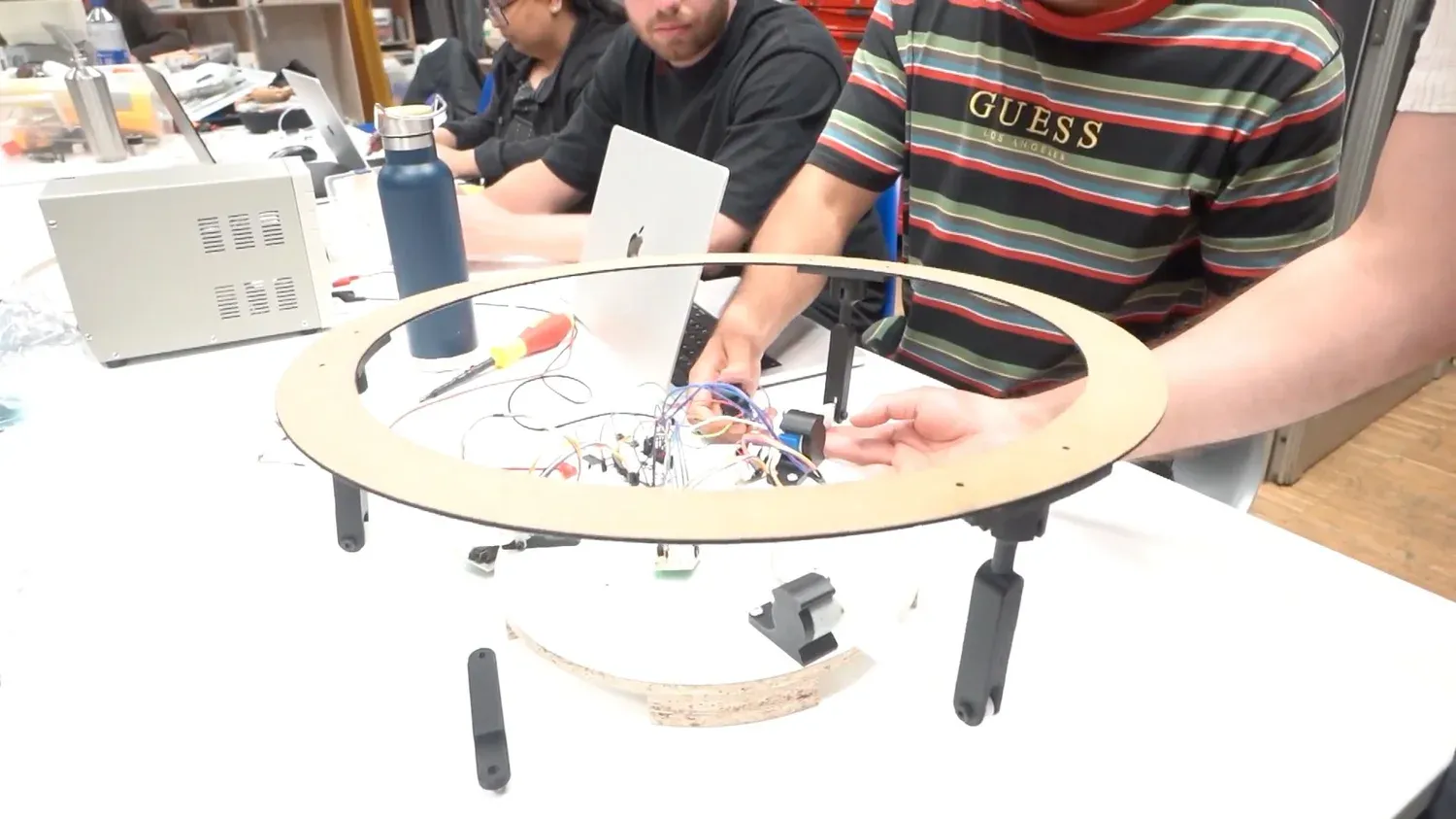 The laser-cut ring held up by three 3D-printed arms ending in ball-socket joints, motors and wiring at the centre