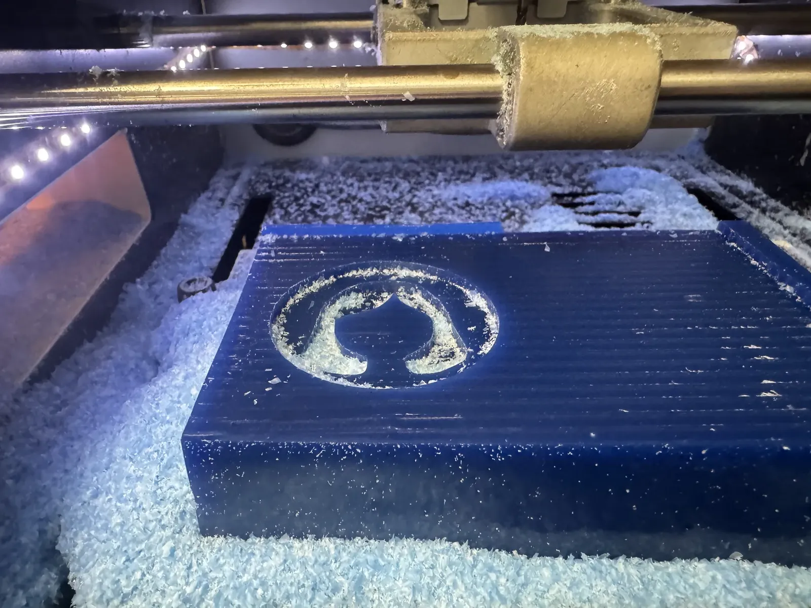 The avatar shape emerging in blue wax mid-roughing, stepped walls visible, chips around the recess