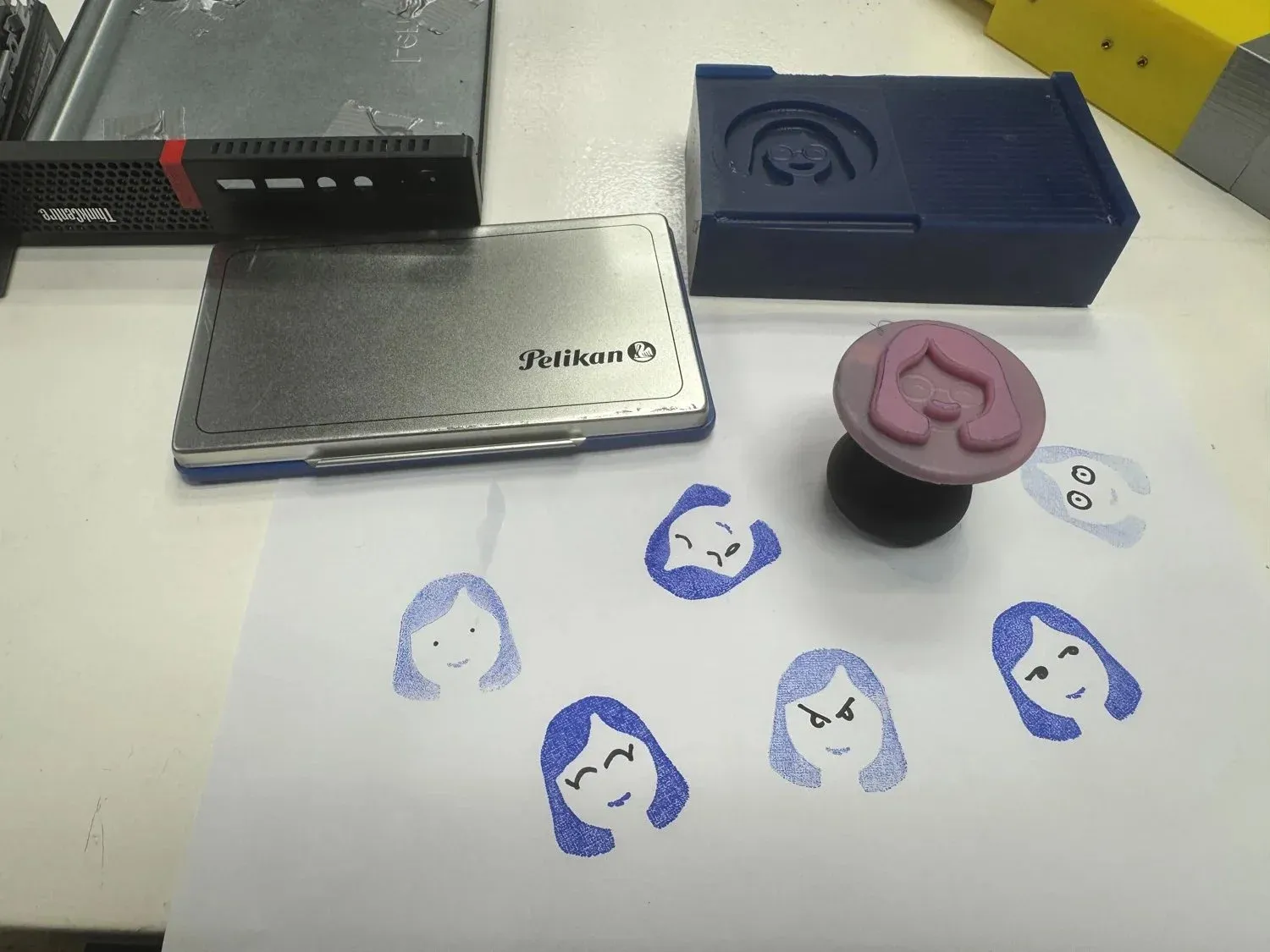 The finished silicone avatar stamp surrounded by its blue-ink impressions on paper, with the milled-wax mold in frame