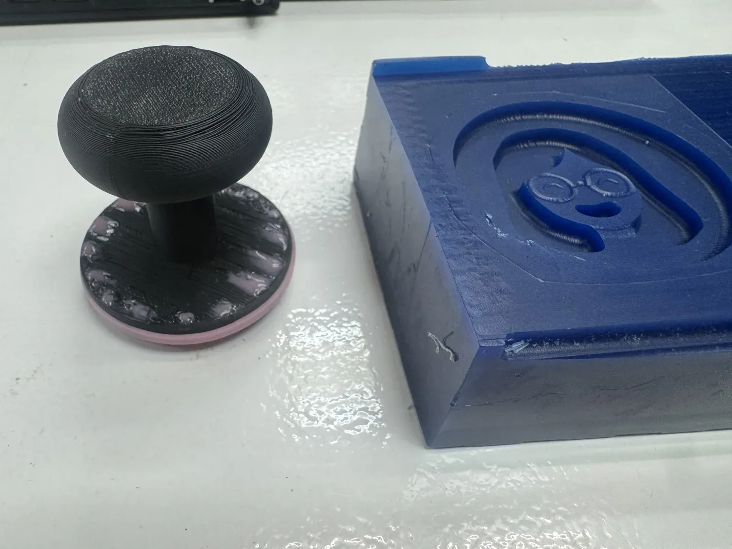 The finished silicone stamp on its 3D-printed handle beside the blue wax mold