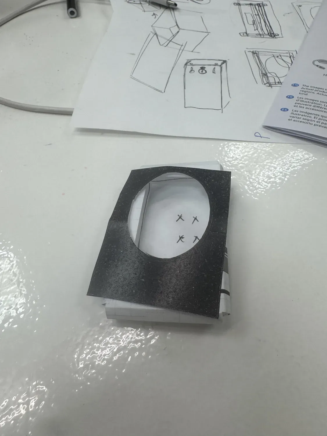 A folded paper maquette of the mirror with concept sketches behind it