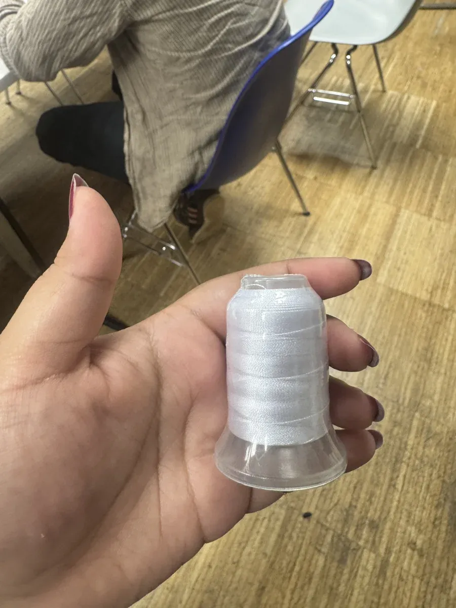 Hand holding white embroidery bobbin thread
