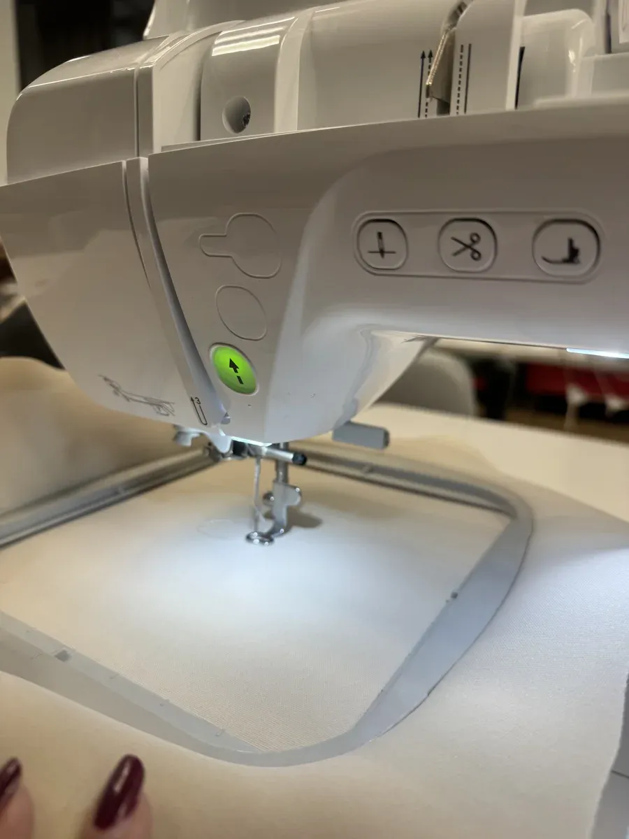 Fabric hooped in embroidery frame with green start button visible