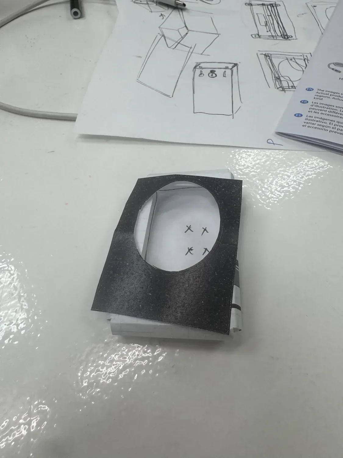 Paper mockup of the oval aperture over a folded body, four VESA mount points marked, chassis sketches behind