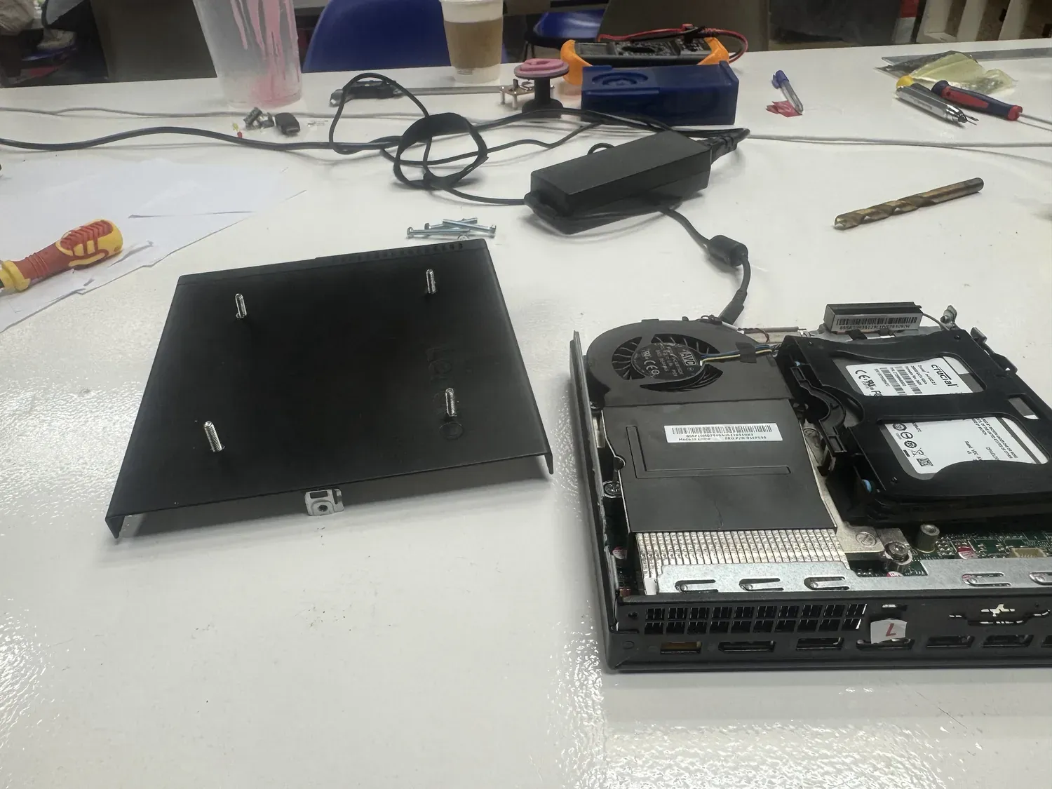 ThinkCentre opened beside its removed cover plate, with VESA screws and a drill bit ready for mounting