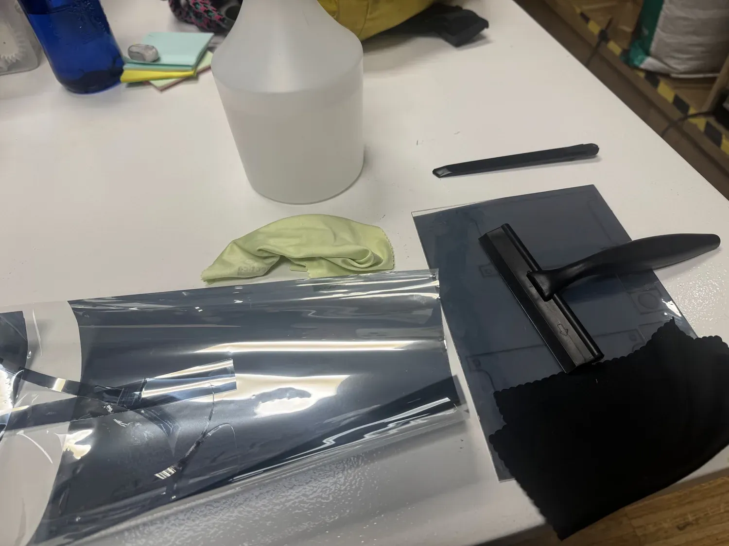 One-way mirror film, squeegee, spray bottle, and microfibre cloth laid out beside an acrylic sheet being filmed