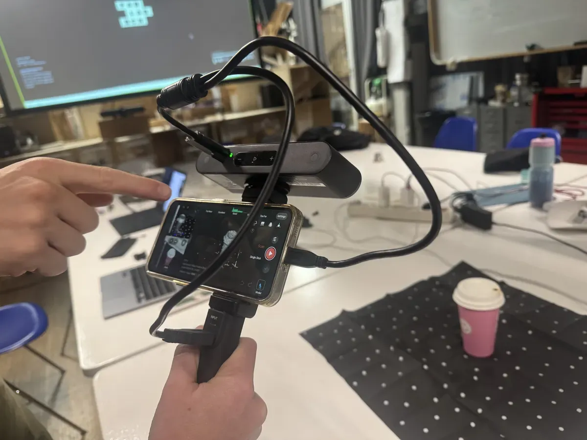 Handheld 3D scanner with phone mount showing real-time scan preview