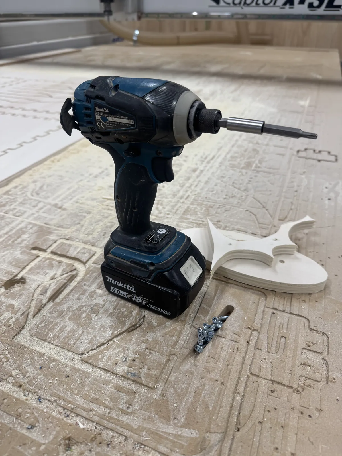 Makita impact driver, screws, and a freshly cut test piece on the bed
