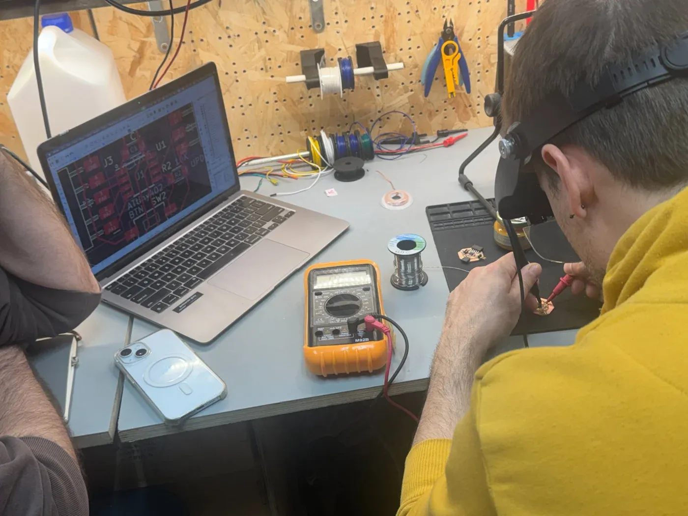 Soldering station, KiCad layout open, multimeter, solder reel, PCB