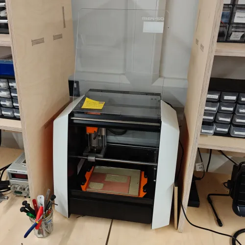 Roland SRM-20 desktop mill with lid open, copper board visible on the bed