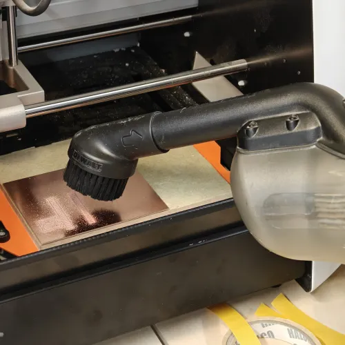 Vacuuming the milled board to clear copper dust and inspect the traces