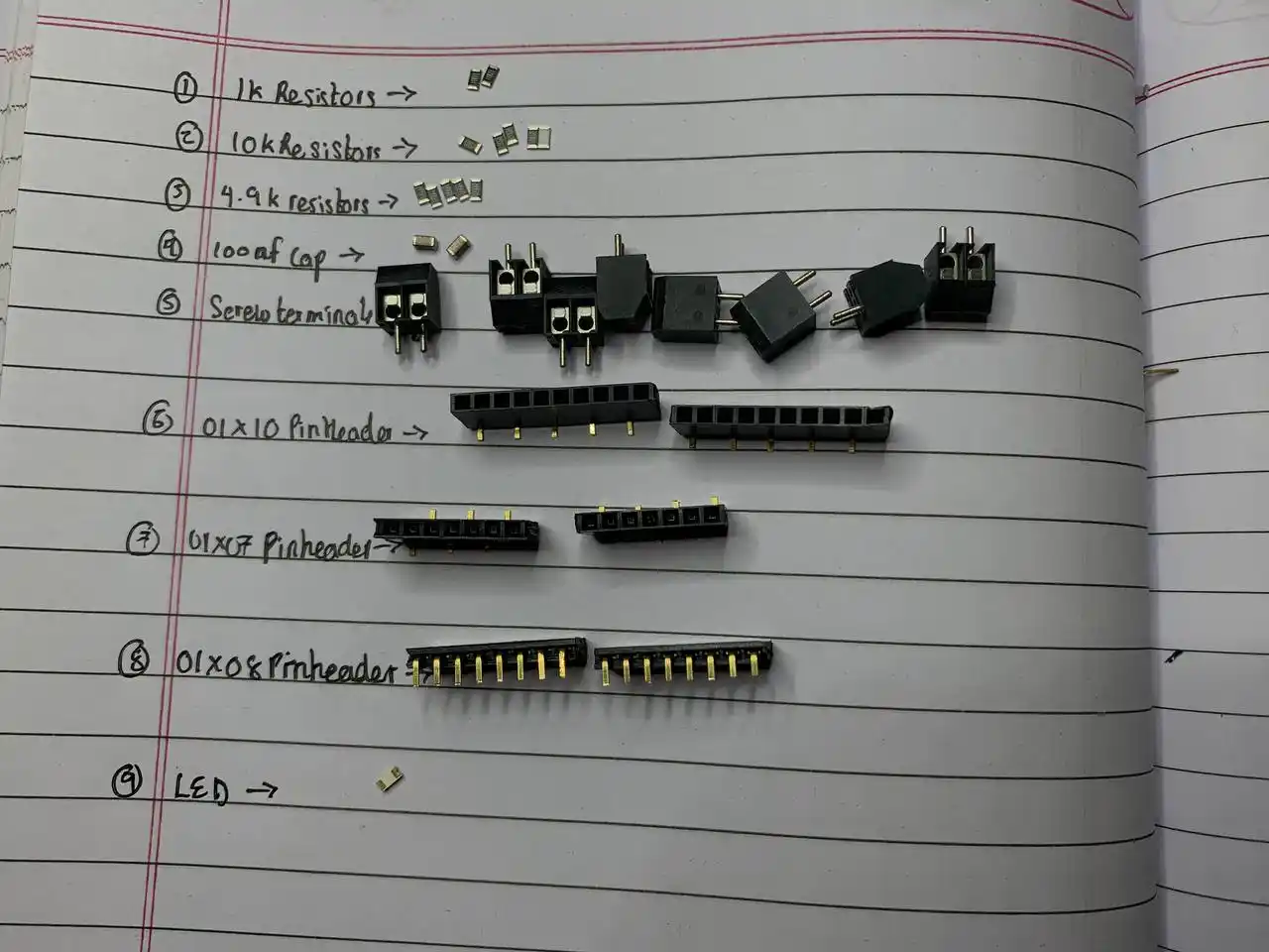 handwritten component list in notebook with SMD components and connectors laid out beside it