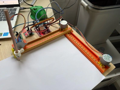 Title: image1.jpeg - Description: The assembled warm-up — our little orange-and-yellow Mini CNC plotter on the bench, hooked up to a laptop.