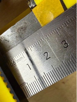 Title: image17.jpeg - Description: Close-up of a steel ruler against the Coloured Plotter's yellow side plate — checking that two reference holes are co-axial before final tightening.