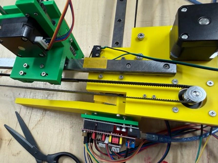 Title: image19.jpeg - Description: Top-down view of the Y-axis sub-assembly — NEMA 17 motor, green carriage, yellow side plate, GT2 belts routed through the pulleys.