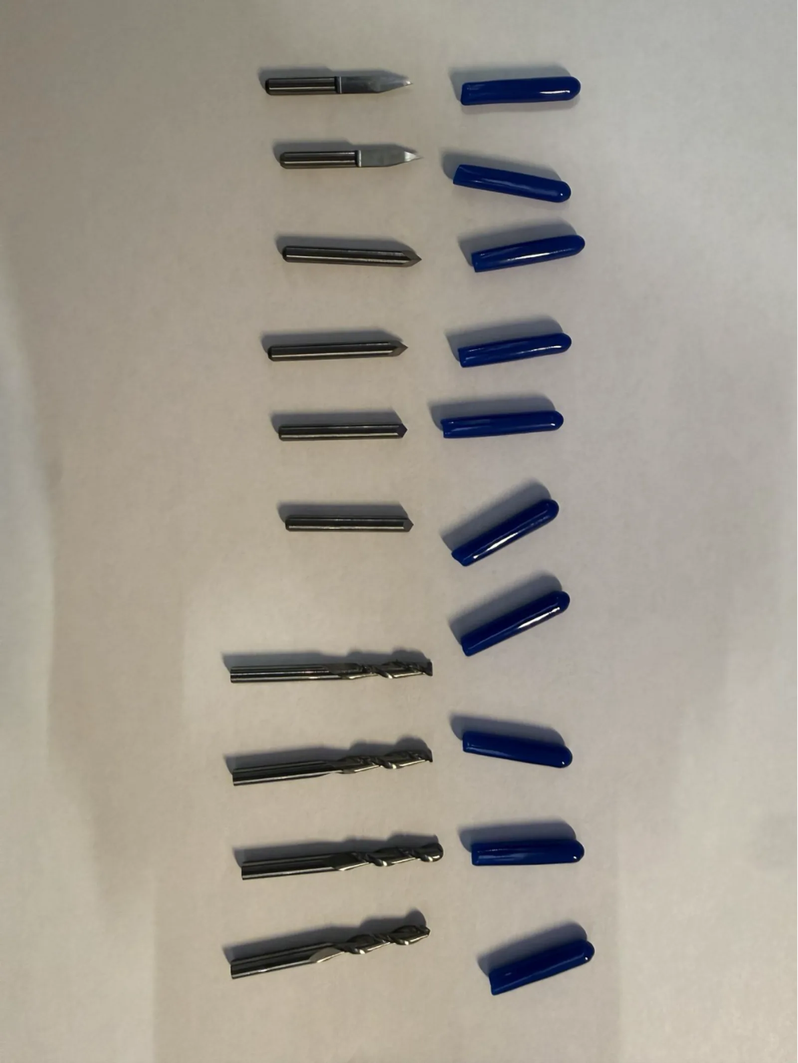 Full set of PCB cutting tools – V-bit engraving bits (left, pointed tips) and spiral end mills (right, fluted), each with blue protective caps