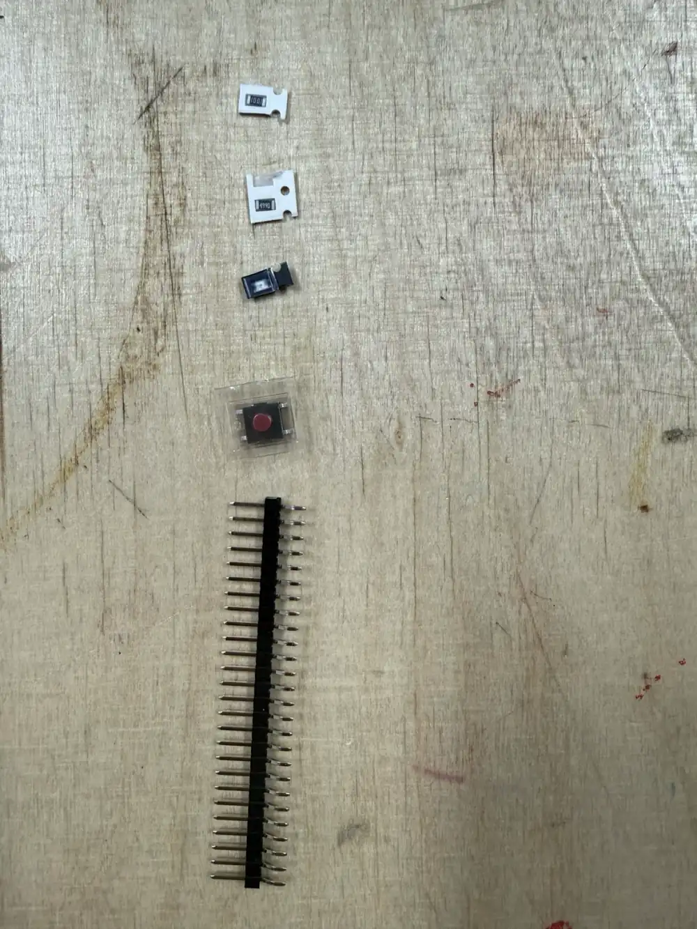 Components laid out before soldering: SMD chip resistors (top), a red tactile button (centre), and a long 40-pin header strip for cutting to size