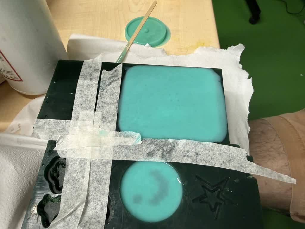 Pouring teal ecoflex into the master mold — window and encoder cavities filling, tape masking the edges