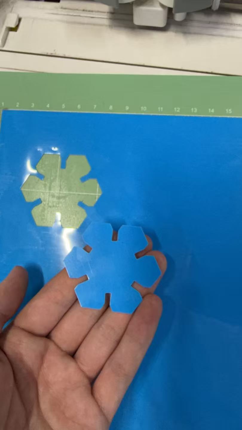Hand holding blue heat-transfer vinyl hex puzzle piece above Cricut mat with cut outline