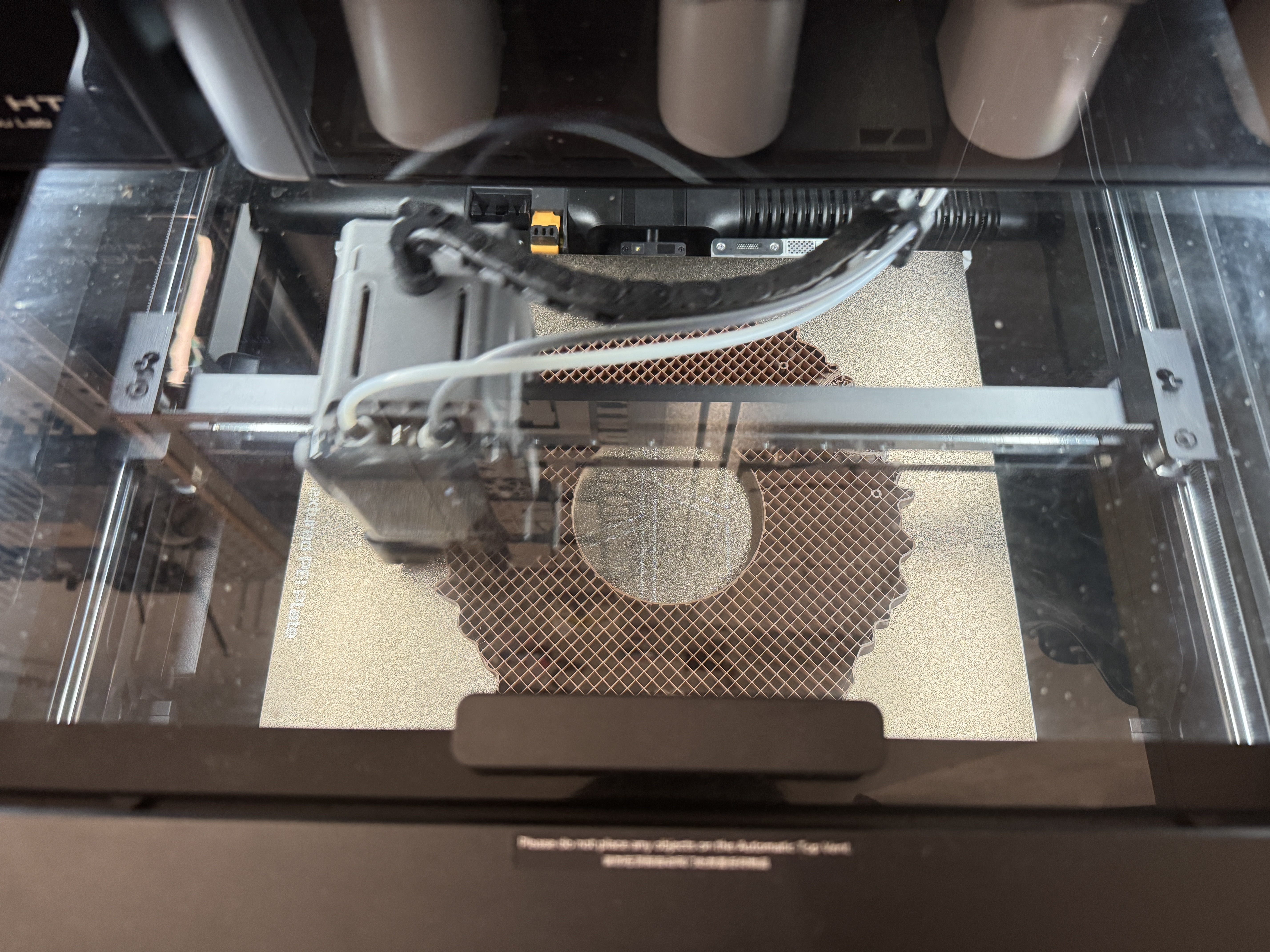 Top view through the printer lid of the second print in progress on a Bambu Lab textured PEI sheet