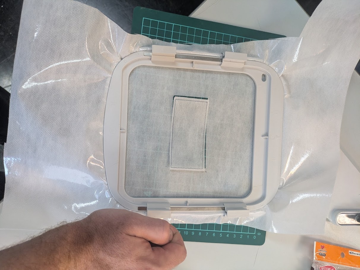 I create a single 1px line rectangle around my design and then sent it to the embroidery machine to determine where the machine would actually be working so I could properly align the t-shirt and the backing material