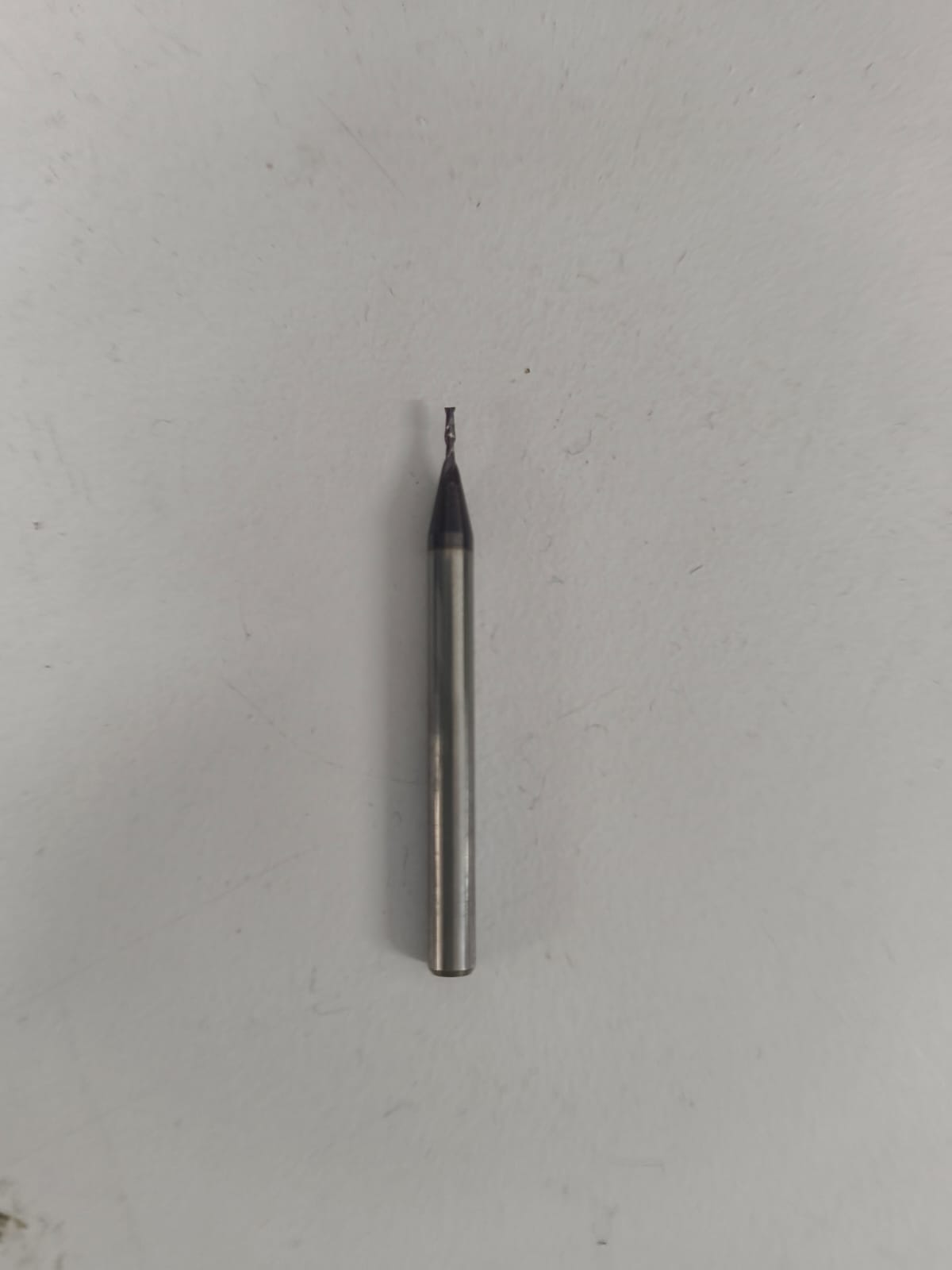 1/32 inch end mill with a dark-coated flat tip on a long cylindrical shank used for drilling and board outline cutting
