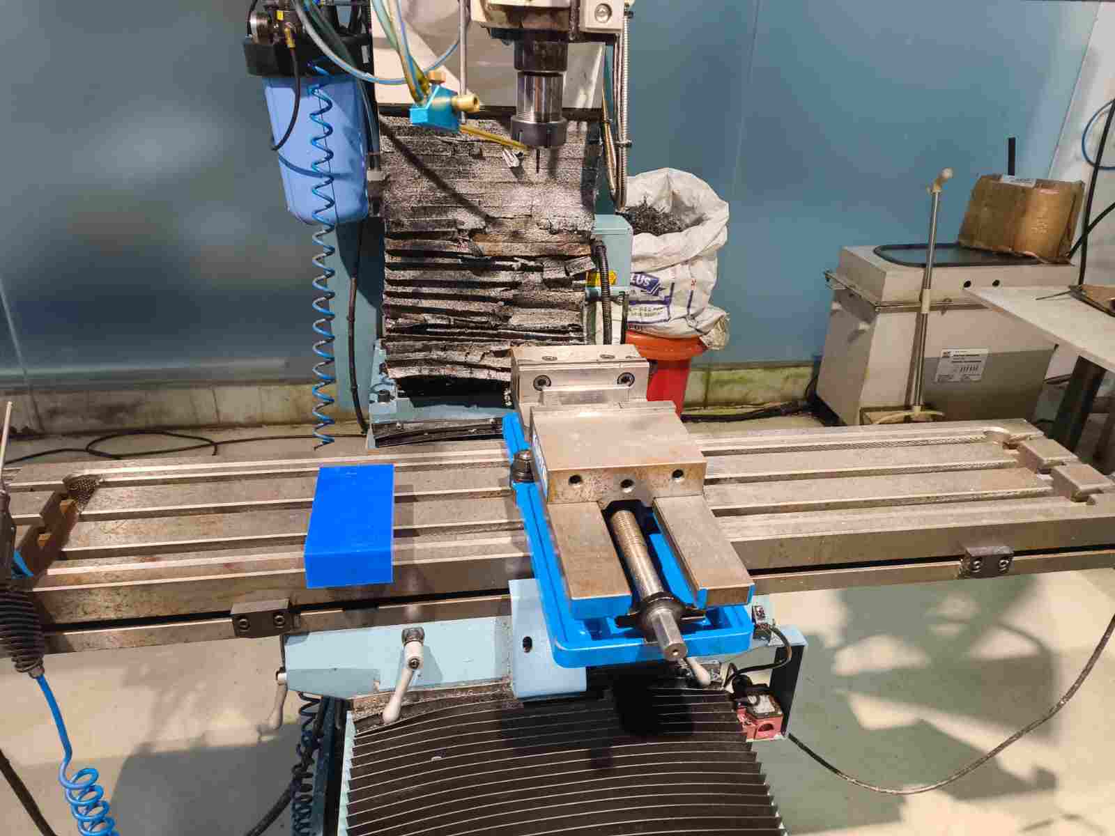 CNC milling machine with blue vise clamped to the table, wax block visible to the left, spindle raised above the work area