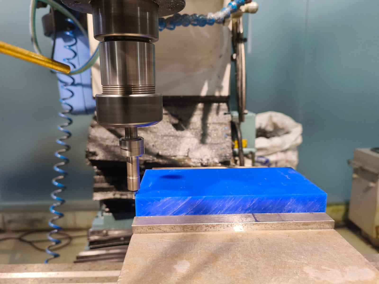 CNC spindle with end mill positioned directly above the blue wax block clamped in the vise, about to begin the first machining pass