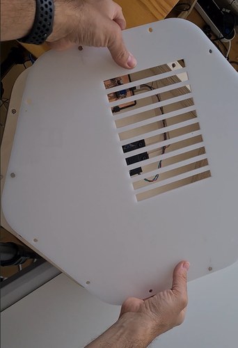 Hands holding the white acrylic bottom cover, a grille of ventilation slots cut over the electronics.