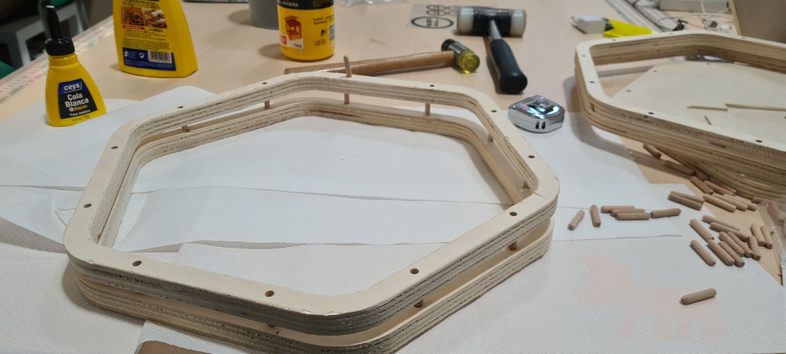 Close view of a glued plywood ring frame with dowels protruding, scattered dowels and a mallet nearby.