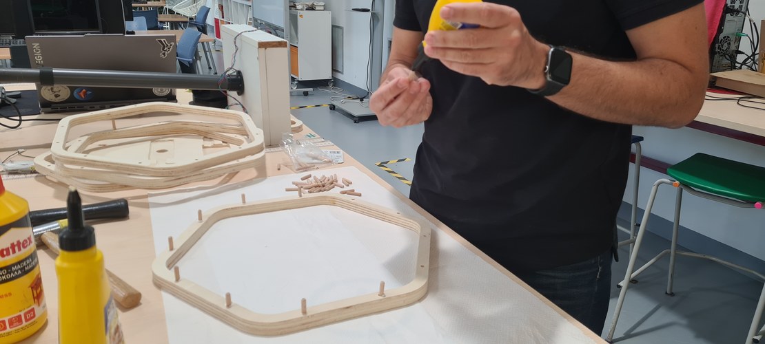 Two plywood ring frames on the lab table with dowels pushed into their edges, glue bottles alongside.