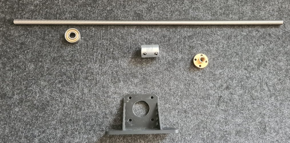 Flat lay of the drive components on grey felt: T8x8 lead screw, 608ZZ bearing, flexible coupling, brass T8 flanged nut, and a printed motor mount bracket.